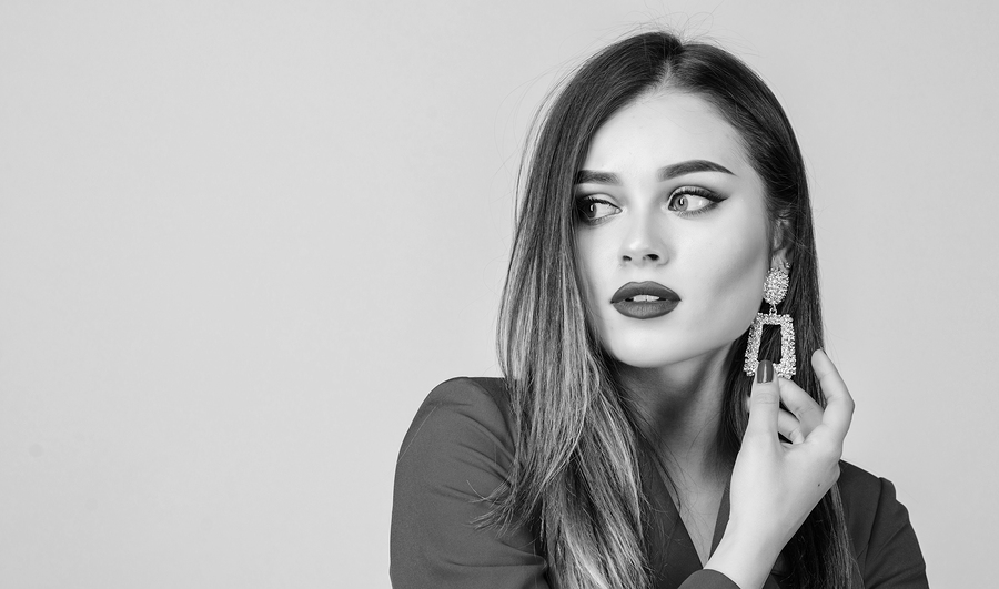 Modetrend. Juwelier. Vorbildliches langes Haar des Mädchens, das goldene Schmuckohrringe demonstriert. Teures Zubehör. Modischer Schmuck. Makelloses Make-up und perfekter Schmuck. Frau tragen glamouröse Ohrringe